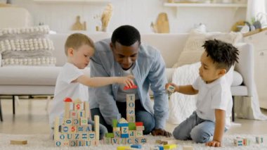 Multiracial persons video. Happy black man playing with children building tower of wooden cubes. Children build tower of cubes sitting on floor of room. Tower of cubes collapses in hands of child.