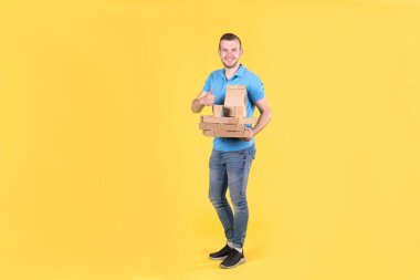 Sırtında termo torbayla restorandan yemek getiren gülümseyen genç adam sarı stüdyo arka planında müşteri siparişi tutuyor. Ofise ya da eve fast food servisi.