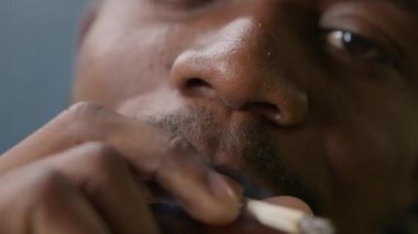 Bad cigarette smoking habit. Concept smoking cannabis, cigarette smoking. Black teenager smokes cigarette with nicotine. Close-up face African American smoking cigarette with marijuana, exhales smoke