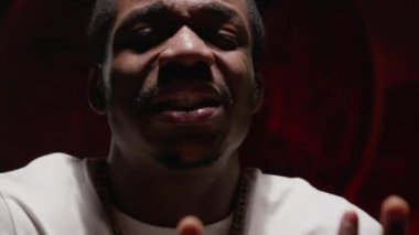 Recording clip for black singer. Emotional performance of song. Portrait singing african american man in white t-shirt emotionally waving his hands at camera on an underground red background