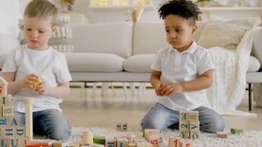 Two children play on floor at home and build towers from wooden blocks. Boy takes cube from friend, frustrated child plays at home. Two children play together with wooden blocks. Children friendship