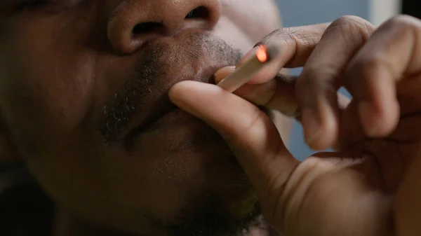 Black teenager smokes cigarette with nicotine. Close-up face African American smoking cigarette with marijuana, exhales smoke. Bad cigarette smoking habit. Concept smoking cannabis, cigarette smoking