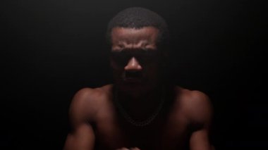 Portrait black African American man with pumped naked torso sings song emotionally waving his arms on black background. Shooting clip of rap artist. Man sings rapping song. High quality 4k footage