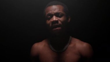 Portrait black African American man with pumped naked torso sings song emotionally waving his arms on black background. Shooting clip of rap artist. Man sings rapping song