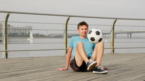Young Freestyler Juggles Ball Sitting Pathway Boat River Sportsman Does — Stockvideo