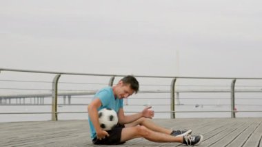 Young man throws and kicks ball lying on empty path. Professional sportsman shows lower body tricks using feet. Male person does juggling smiling to himself