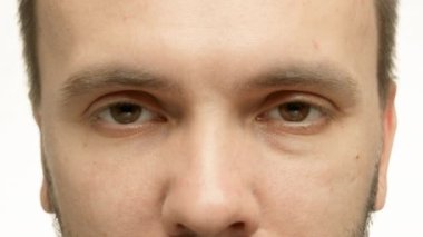 Face of serious adult man opening eyes. Middle-aged brunet has brown eyes with wide thick eyebrows. Man with dark hair blinks on white studio background closeup