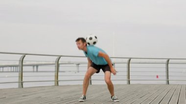 Young freestyler in blue t-shirt shows upper body tricks. Stylish man uses shoulders and hands together by handrail. Guy juggles ball throwing from shoulders to head