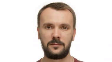 Portrait of middle-aged man with short dark hair and brown eyes. Man with well-groomed beard and mustache stands blinking in white studio without showing emotions