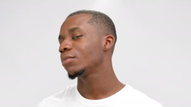 Young African-American man in white wearing turns head smiling. Portrait of dark-haired person with small goatee beard against white studio wall closeup