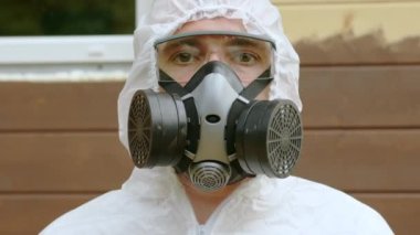 Portrait of man professional painter in protective suit, glasses and respirator looking at camera on painted wooden facade wall background. Repair construction finishing works, renovation concept.
