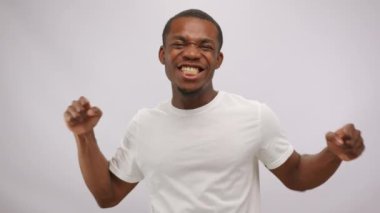 Young black man wearing white t-shirt looks with excited and happy expression smiling. African American guy shows performance with positive emotions at wall