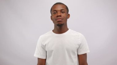 Young black guy shows disagreement with upset and disappointed expression. African American man wants to share opinion and thoughts at white studio wall