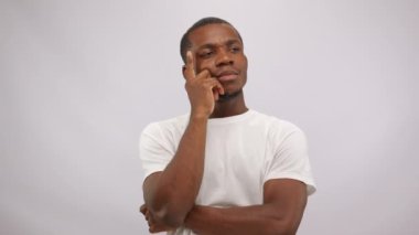 African American man thinks about awesome idea looking puzzled. Interesting thought hits young cast member with short haircut. Guy shows thumb-up in white studio