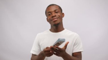 African American man shows bunch of cash salary for work performing sketches at audition. Cast member demonstrates positive emotions with toothy smile at white studio wall