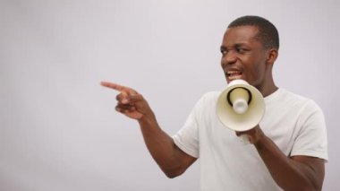 African American man in white t-shirt yells holding megaphone. Young cast member demonstrates sketch about protest in environment defense screaming at white wall