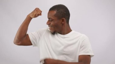 African American man demonstrates power and strength showing muscles. Strong black guy enjoys looking sporty and strong demonstrating biceps in white studio