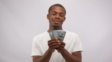 African American man shows bunch of money with happy expression. Young actor enjoys monthly salary working at favourite job. Guy demonstrates toothy smile