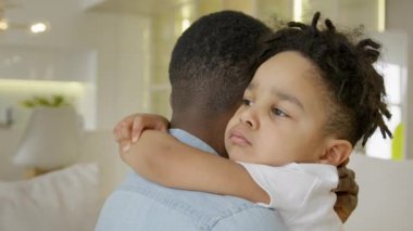 Happy multiracial family of father and son. Multiracial boy embraces a black African-American father and looks into camera. Hugs of father and 3-year-old son sitting on couch at home
