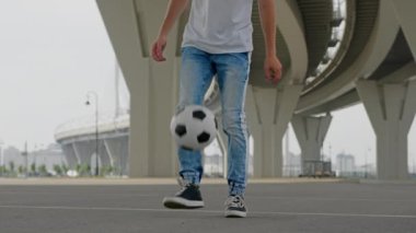 Man professional footballer is performing tricks with ball in freestyle training on city street near the bridge. Soccer player is practicing training outdoors juggling ball improving sport skills.