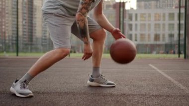 Man in sportswear shorts and t-shirt is practicing exersice hitting basketball ball training on court in city at summer day. Improving Sports basketball skills concept. Outdoors modern urban life.