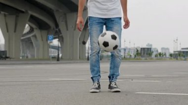 Man wearing black jeans and black sneakers show tricks using lower body. Sportsman throws ball and juggles with toes. Person demonstrates juggling under trestle