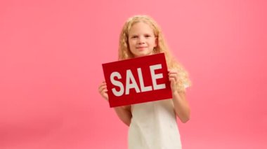 Slow motion portrait cheerful teenage girl in white T-shirt dances and smiles holding red banner with inscription sale on studio background. Girl advertises big sale on Black Friday and big discount