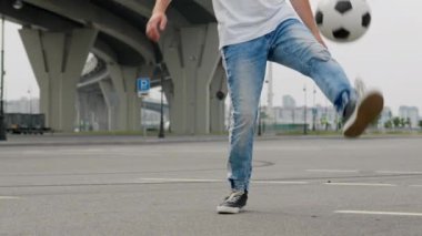 Sports and football skills concept. Man professional soccer player in jeans practicing kicks tricks with ball, legs close-up. Footballer is training outdoors juggling ball, freestyle in slow motion.