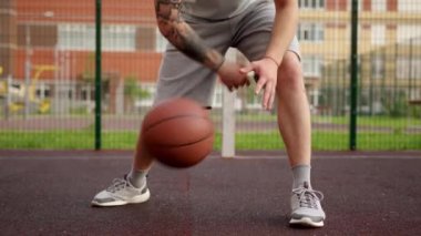 Unrecognizable man basketball player is bouncing hitting ball using both hands in freestyle on playground in slow motion on city street. Outdoors training, improving sport skills concept.