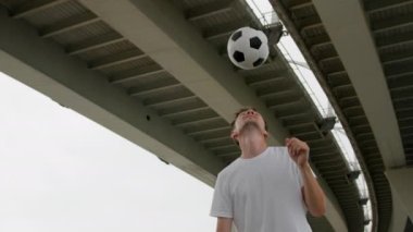Man soccer player is practicing tricks bouncing ball on head honing his skills in city. Professional footballer is training, warming-up outdoors in freestyle. Sports and football skills concept.