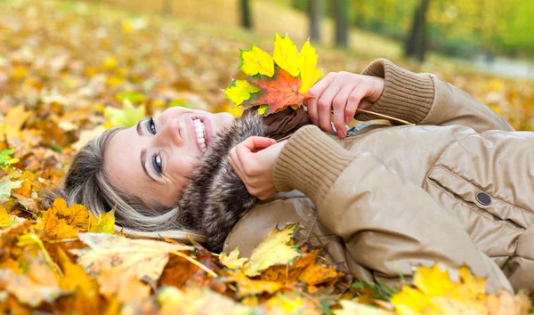 Junge lächelnde Frau liegt im Herbst auf Blättern — Stockfoto