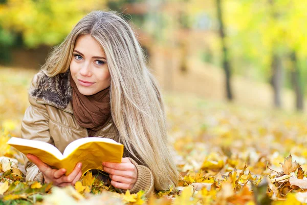 Pretty young woman reading in a park in autumn — Stock Photo, Image