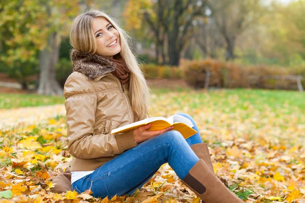 Lächelnde Frau liest im Herbst im Park — Stockfoto