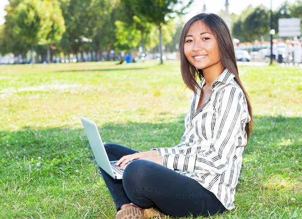 Mujer asiática escribiendo en un portátil en un parque — Foto de Stock