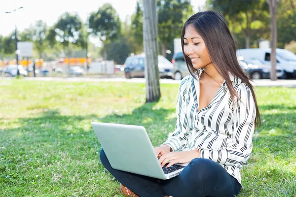 Asiática chica usando un portátil en un parque — Foto de Stock