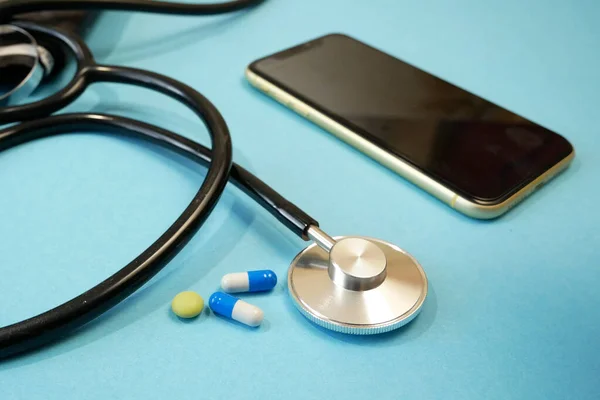 青い背景のスマートフォン上の丸薬と聴診器 遠隔医療や電子健康の概念 — ストック写真