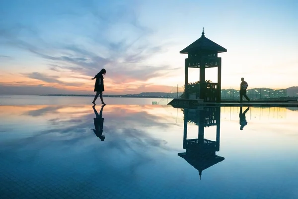 man and woman silhouettes coming in the rays of the setting sun on landscape of beautiful infinity pool and sea and oriental gazebo. Love story, valentine\'s day
