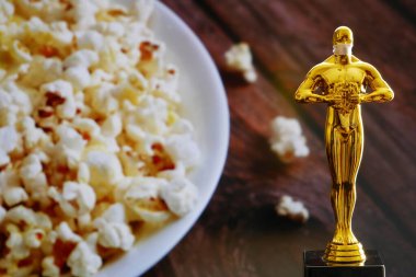 Hollywood Altın Oscar Akademisi, patlamış mısır arka planında tıbbi maskeli bir heykel. Başarı ve zafer kavramı. Koronavirüs zamanında Oscar töreni, yakın çekim.