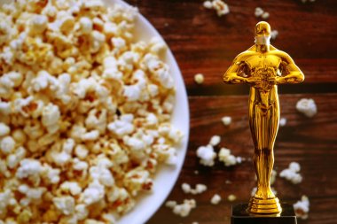 Hollywood Altın Oscar Akademisi, patlamış mısır arka planında tıbbi maskeli bir heykel. Başarı ve zafer kavramı. Koronavirüs zamanında Oscar töreni, yakın çekim.