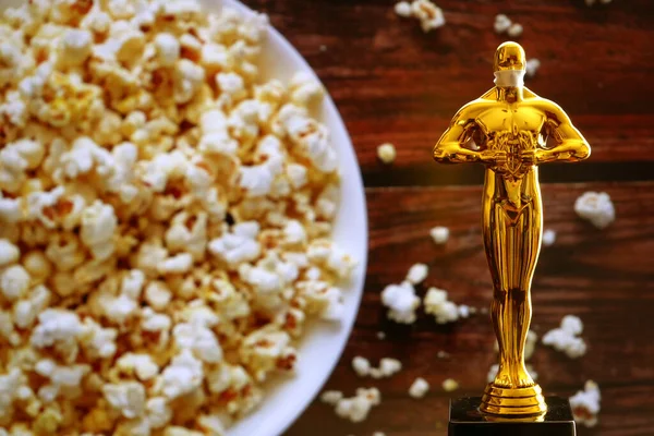 Hollywood Altın Oscar Akademisi, patlamış mısır arka planında tıbbi maskeli bir heykel. Başarı ve zafer kavramı. Koronavirüs zamanında Oscar töreni, yakın çekim.