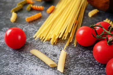 Çeşitli makarna türleri (fusilli, penne, cavatapi, cannelloni, spagetti) siyah arka plan, çiğ makarna seti ve domates, set, koleksiyon, kapanış