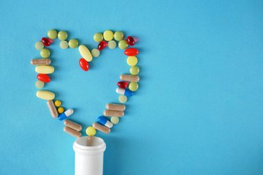 Mavi arka planda kalp ve beyaz şişe olarak ilaçlar, haplar ve kapsüller, Şubat ayındaki Amerikan Kalp Kapsülü