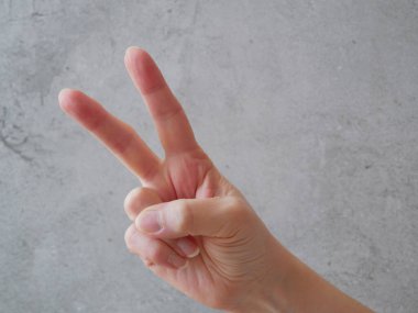 Zafer, el hareketi. Gri arka planda iki parmak havada. Barış, özgürlük işareti. El hareketi V işareti. Yakın çekim.