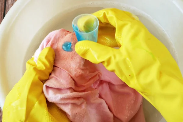 Çamaşırları elle temizliyorum. Eldiven giymiş kadın elleri lekeli bezleri leke çıkarıcı ile yıkıyor ve sabunlu suya batırıyor, yakın plan.