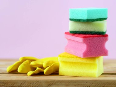 Mutfakta ahşap arka planda bir sürü renkli sünger ve sarı eldiven var. Temizlik malzemeleriyle dolu sepet, yakın plan.