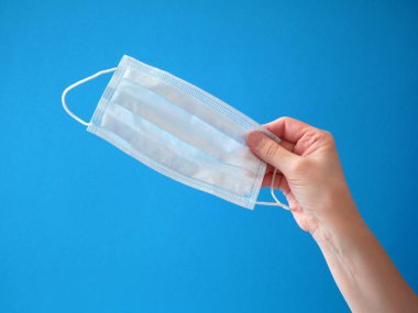 Mavi arka planda yüz maskesi tutan bir kadın. Virüs yaymak için koruyucu raspiratuar maskesi. Yakın çekim.