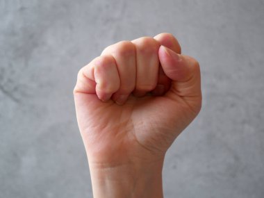 Gri arka planda erkek yumruğu. Protesto, zafer, güç ve güç için elini kaldırdı. Sayma, saldırganlık, cesur kavram. Yaklaş.