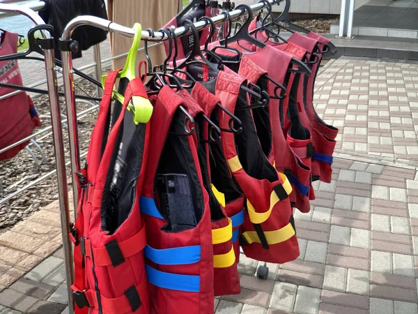 Personal red life vests in store. Many life jackets hang in a row on hangers. Protective safety clothing at rental boat store or shop, outdoors