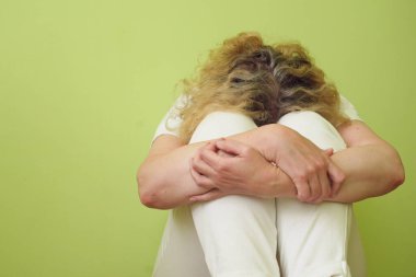 Orta yaşlı bunalımlı bir kadın evde ya da hastanede elleri ile yerde oturuyor. Yalnız, üzgün, negatif duygu ve akıl sağlığı konsepti. Kapalı