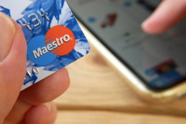 Bir elin Mestro 'dan MasterCard' ı tutarken diğer elin cep telefonunu internet alışverişi, online ödeme konsepti ve yakın çekim için kullanıyor.